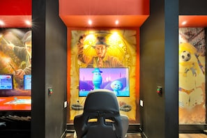 A gaming room with a large screen, gaming chairs, and themed wall art. - 5BR Bear's Den Estate Private Pool & Game Room (Kissimmee)