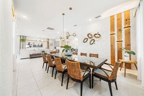 A modern dining area with a white brick wall, wooden accents, and a central table with chairs. - 5BR Bear's Den Estate Private Pool & Game Room (Kissimmee)