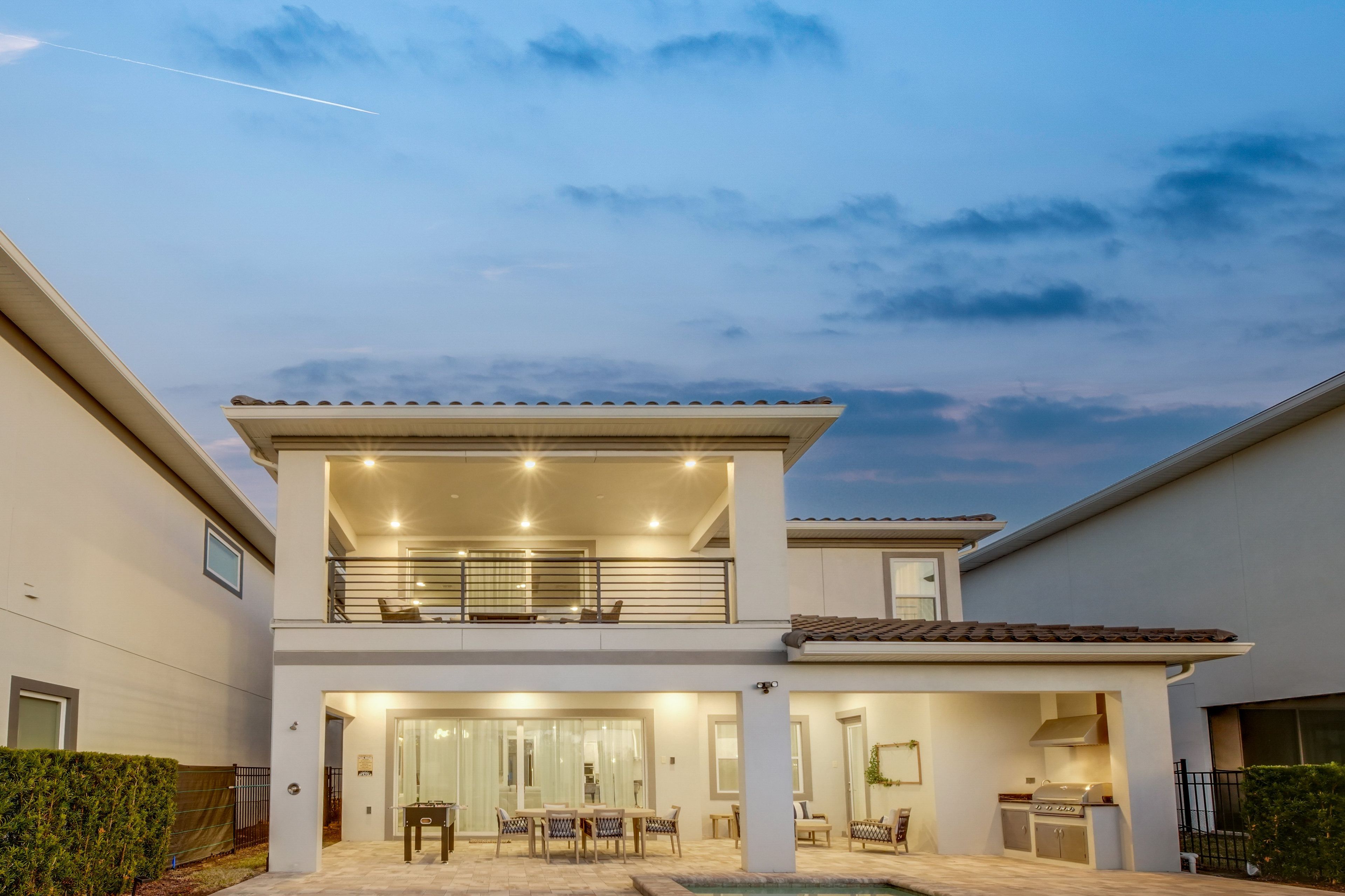 A two-story house with a balcony, a patio with outdoor furniture, and a swimming pool.