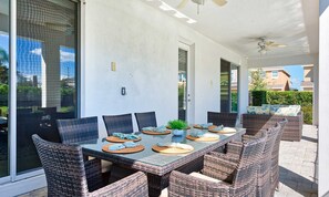 A covered patio with a glass-top table, wicker chairs, and a ceiling fan. - 9BR Encore Villa Custom Design & Game Room (Kissimmee)