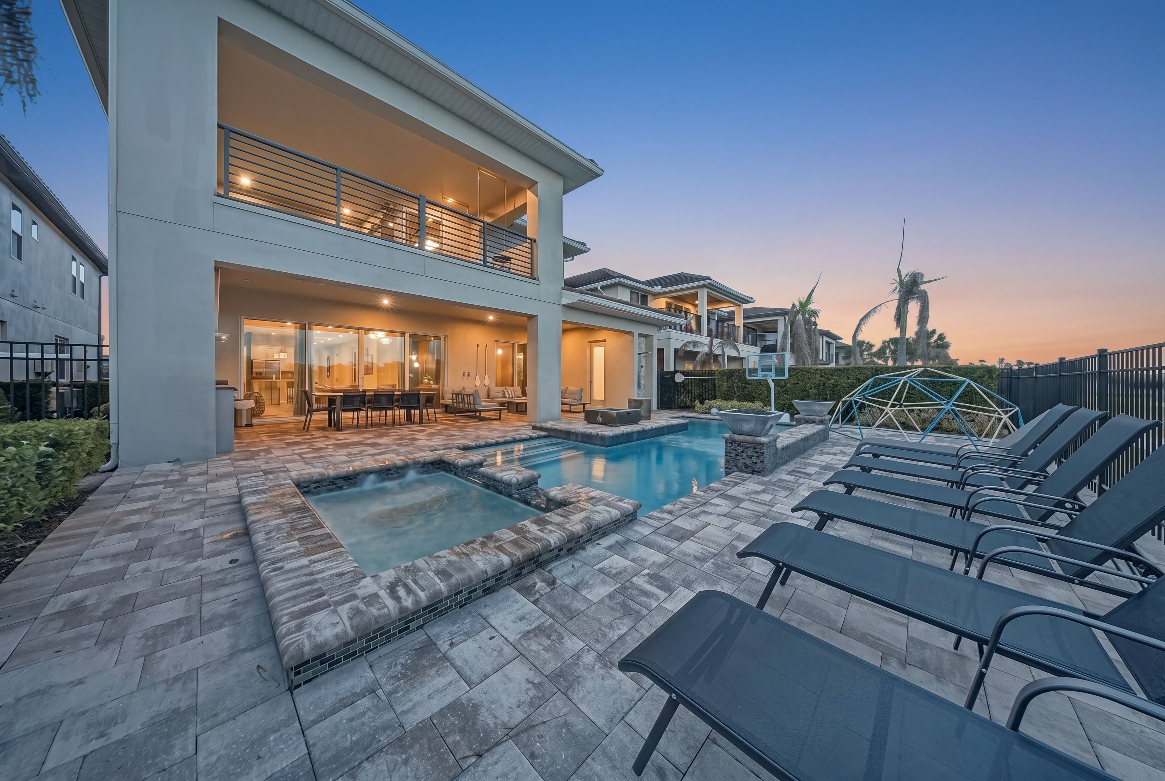 A modern two-story house with a swimming pool, outdoor seating, and a well-lit patio area.