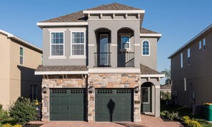 A two-story house with a stone facade, two green garage doors, and a small balcony. - 5BR Encore Villa With Billiards Loft & Pool (Kissimmee)