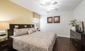 Ein Schlafzimmer mit Bett, Nachttischen, Deckenventilator, Fernseher und gerahmten Kunstwerken an der Wand.