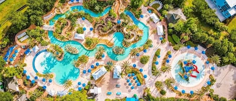 An aerial view of a resort with multiple swimming pools, lounge areas, and palm trees.