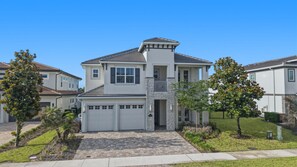 A two-story residential house with a garage, stone facade, and a clear blue sky. - 6BR Bear's Den Estate Pool & Blacklight Arcade (Kissimmee)