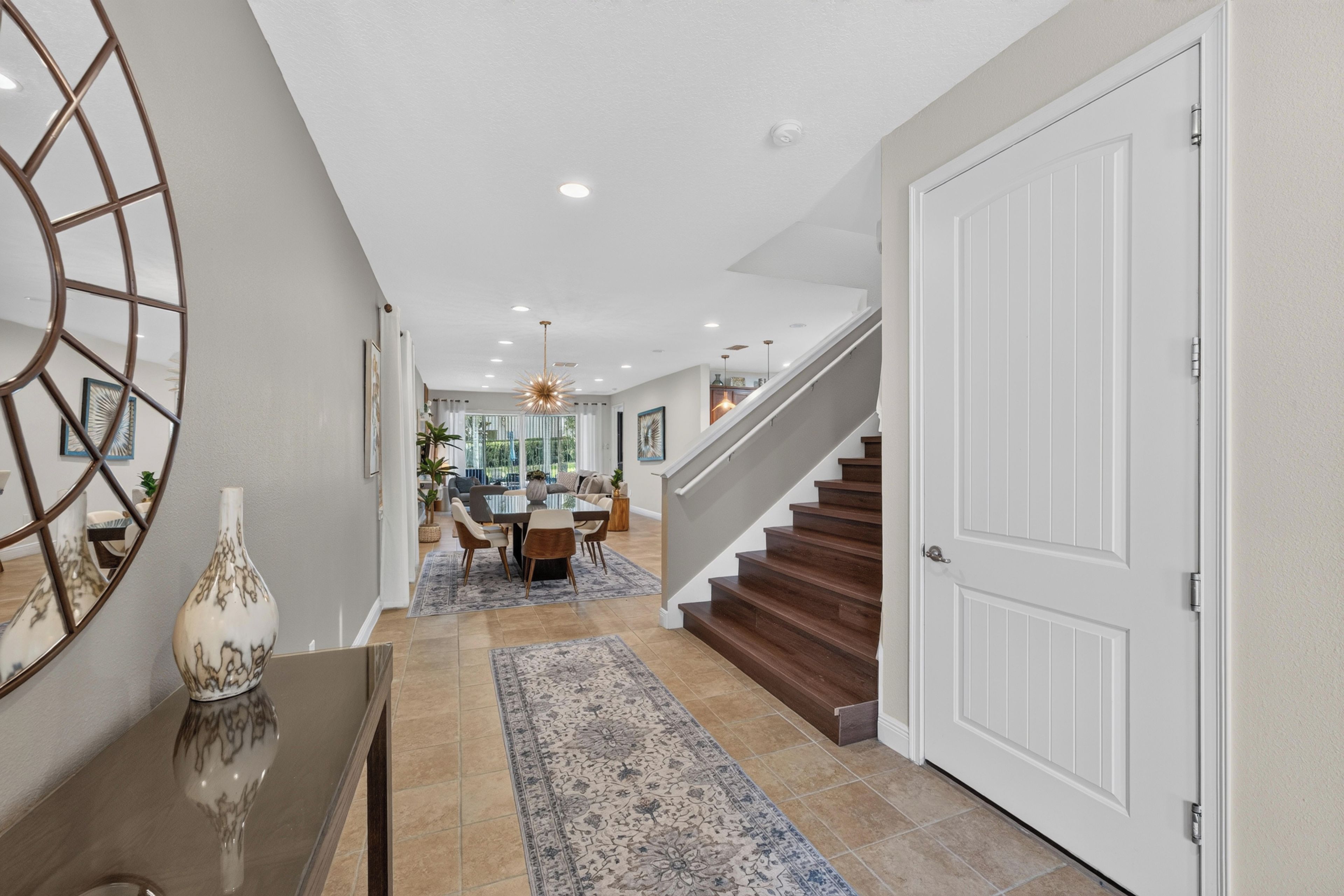 A modern interior with a dining area, staircase, and a hallway leading to a door.