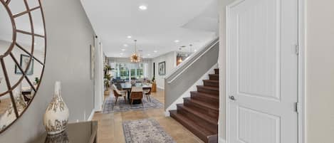 A modern interior with a dining area, staircase, and a hallway leading to a door.