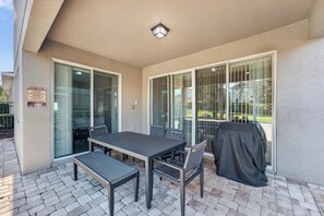 An outdoor patio with a table and chairs, a covered grill, and a glass door leading to a pool area. - 6BR Encore w/ Under-the-sea Kids' Room & Pool (Kissimmee)