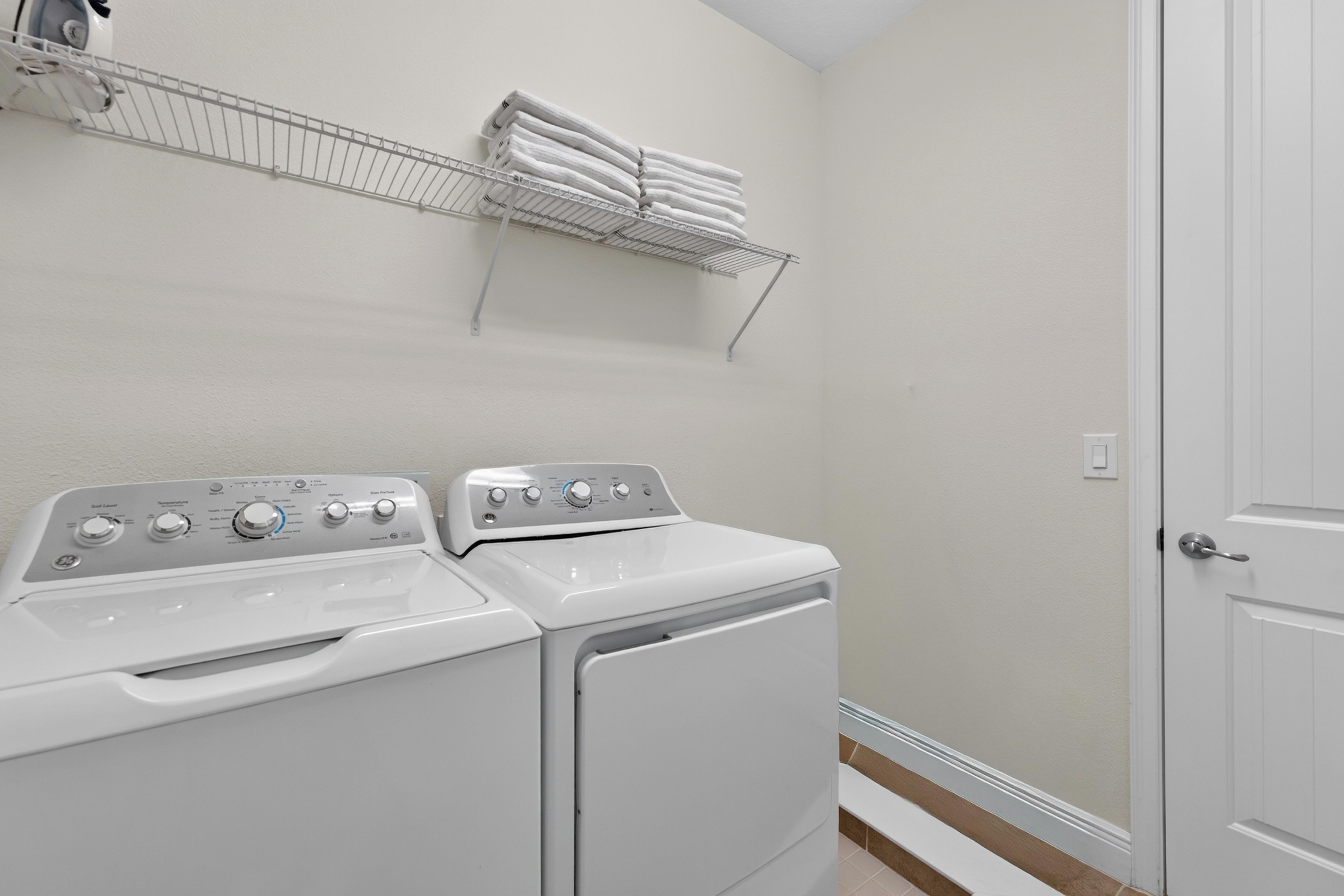 A laundry room with two stacked washing machines and a drying rack above them.
