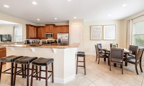 A modern kitchen with wooden cabinets, a stainless steel refrigerator, and a dining area with a table and chairs. - 6BR Encore Villa Pool, Spa & Game Room (Kissimmee)