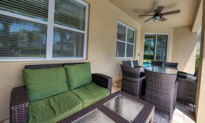 An outdoor patio area with a green cushioned sofa, wicker chairs, and a glass-top table. - 6BR Encore Villa Pool, Spa & Game Room (Kissimmee)