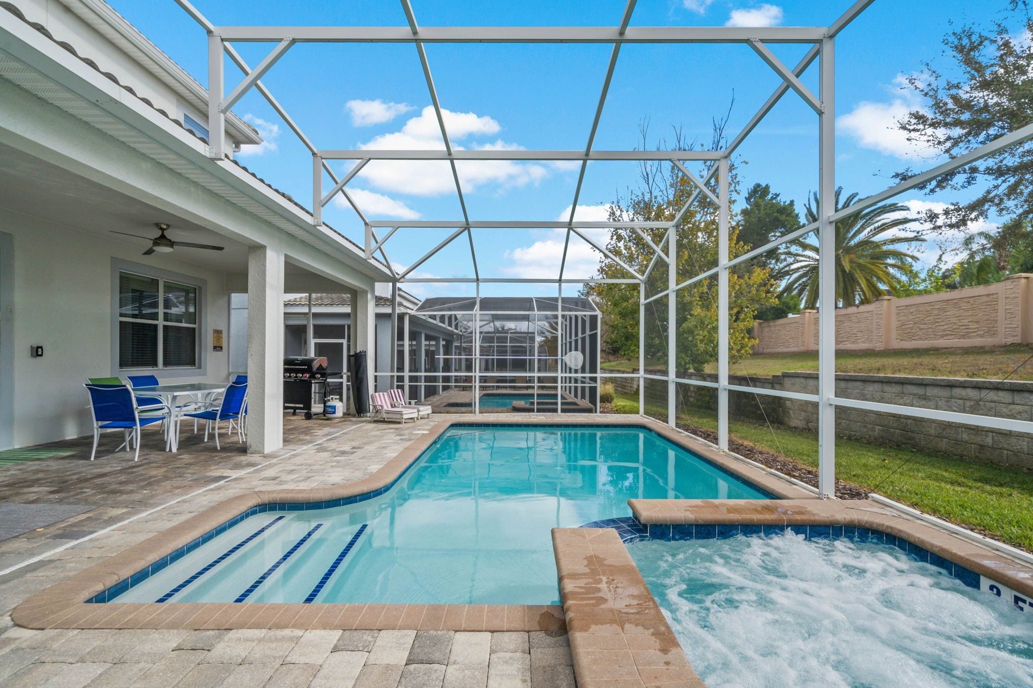 Ein Swimmingpool mit Whirlpool, umgeben von einer überdachten Terrasse mit Stühlen und einem Grill.