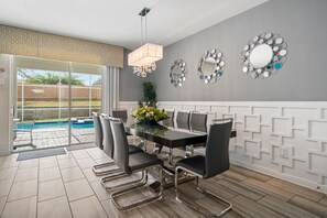 A dining area with a pool view, modern furniture, and decorative wall mirrors. - 8BR Championsgate Villa Theater, Pool & Games (Davenport)