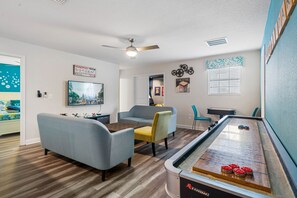 Een woonkamer met een bank, stoelen, een salontafel, een televisie en een jeu de boules tafel.