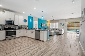 A modern kitchen with a central island, white cabinetry, and a dining area with a view of a pool. - 8BR Championsgate Villa Theater, Pool & Games (Davenport)