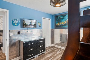 A room with a blue wall, a metal diamond plate backsplash, a black metal cabinet with drawers, a white door, and a framed picture of a castle. - 8BR Championsgate Villa Theater, Pool & Games (Davenport)