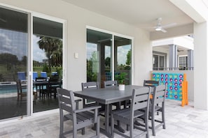 Un patio al aire libre con una mesa, sillas, un ventilador de techo y vistas a una piscina.