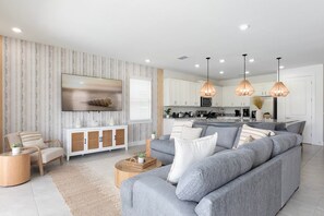 A modern living room with a grey sofa, a wooden side table, and a flat-screen TV mounted on the wall. - Bohemian Chic Oasis With Themed Bedrooms at Reunion (Kissimmee)