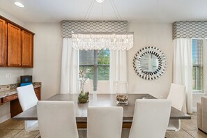 Ein Essbereich mit Tisch, Stühlen, einer Chandelierleuchtre, einem Zier-Spiegel und Blick ins Grüne.