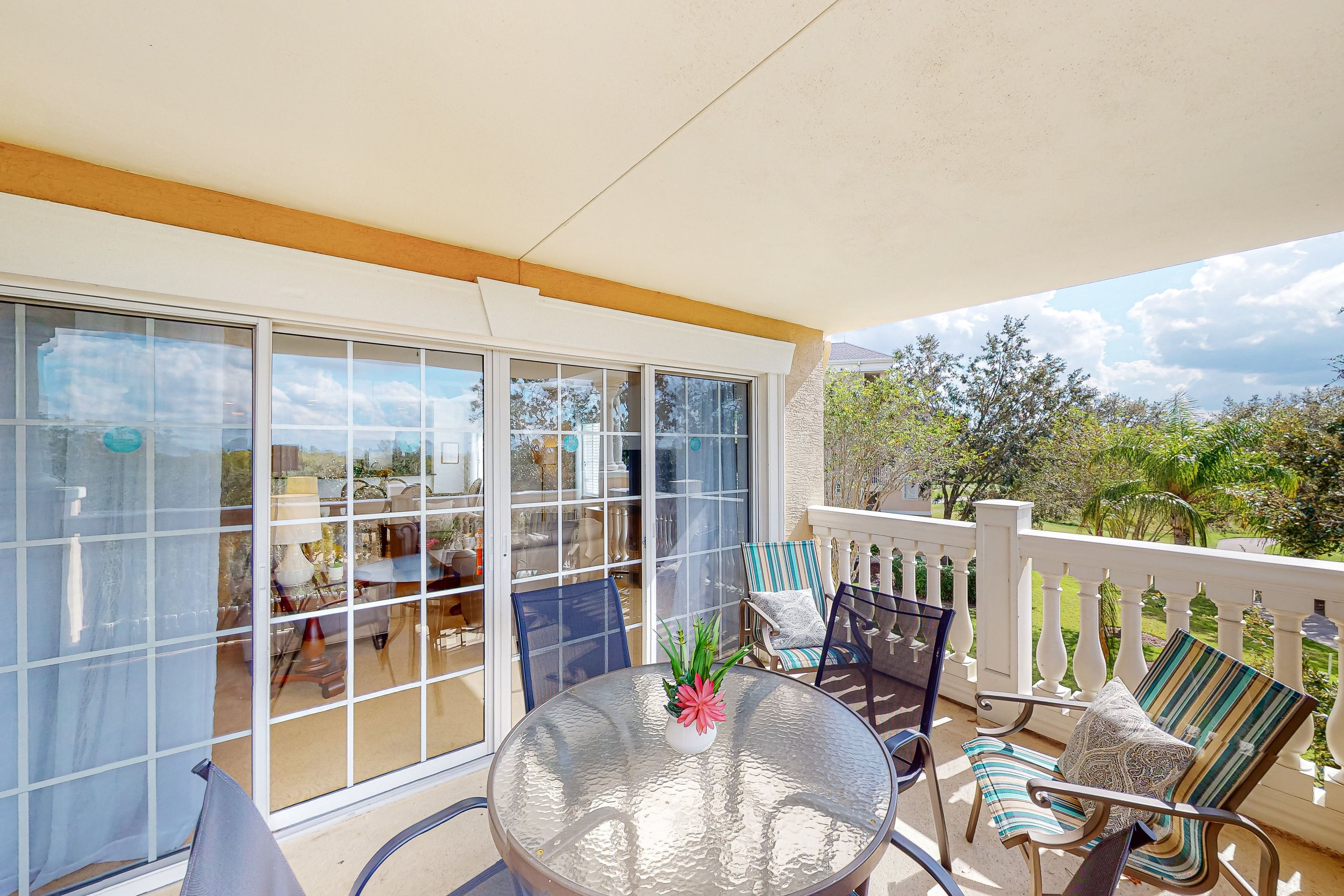 A covered outdoor area with a glass door leading to a patio, furnished with a round table, chairs, and potted plants.