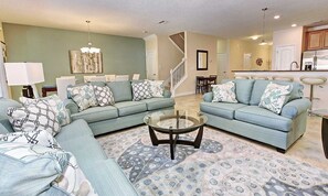 Ein Wohnzimmer mit zwei hellblauen Sofas, einem Glastisch und gemusterten Teppichen.