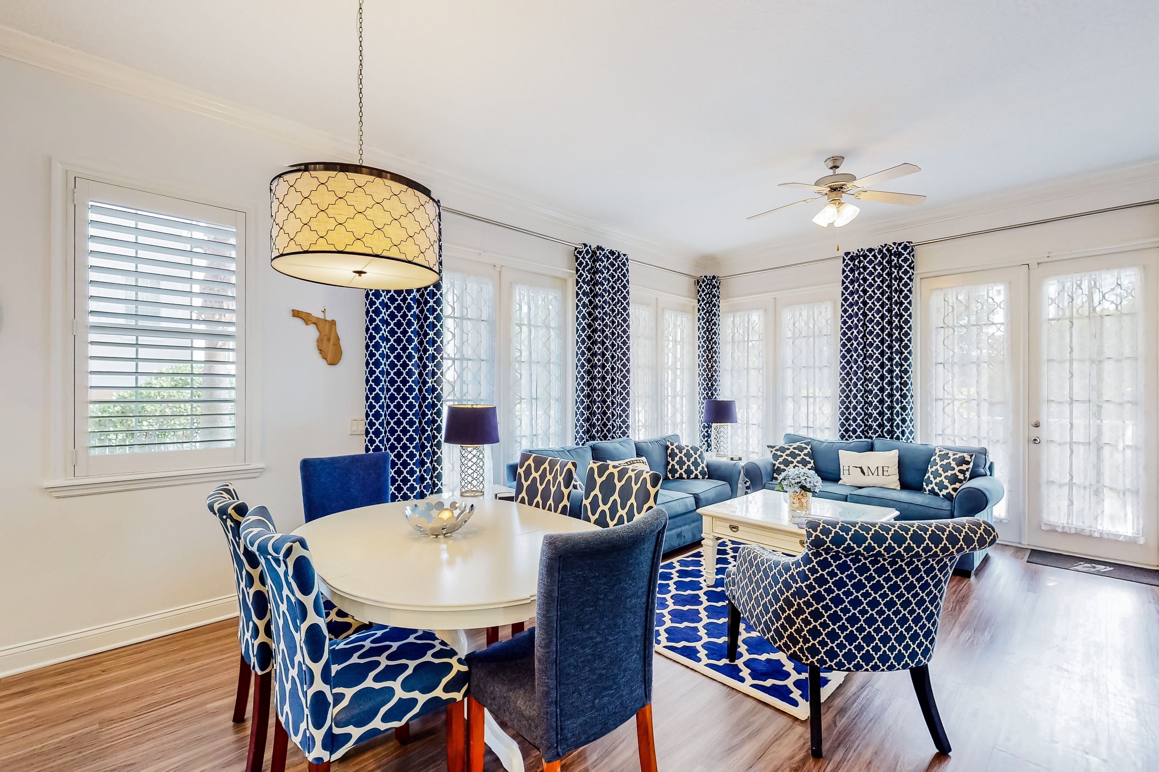 A dining area with a round table, blue patterned chairs, a ceiling fan, and a decorative wall piece.