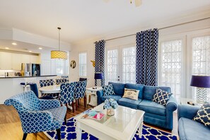 A modern living room with a blue sofa, matching chairs, a coffee table, and patterned curtains. - Elevated Condo With Wraparound Porch at Reunion (Kissimmee)