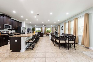 A modern kitchen with dark cabinets, a granite countertop, and a central island with bar stools. - 9BR Encore Villa Pool, Spa & Water Park (Kissimmee)