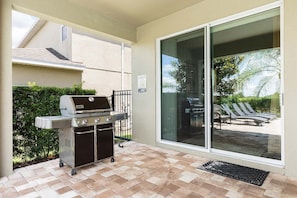 An outdoor patio with a grill, a sliding glass door, and a view of a pool area with lounge chairs. - 9BR Encore Villa Pool, Spa & Water Park (Kissimmee)