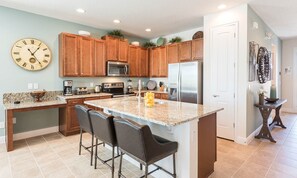 A kitchen with wooden cabinets, granite countertops, a stainless steel refrigerator, a microwave, and a coffee maker. - Cheerful Estate With Water Park Views in Encore (Kissimmee)