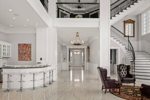 Ein geräumiges Foyer mit hoher Decke, einer imposanten Treppe, einem Barbereich mit Hockern und einer Kristallleuchter.
