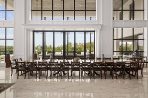 Un vaste espace dédié à la salle à manger, avec une grande table et des chaises, de grandes fenêtres et une vue sur la verdure environnante.