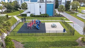 A playground with slides and climbing structures, surrounded by a fence, with a picnic table and benches nearby. - 5BR Reunion Resort Condo With Elevator and Share Pools (Kissimmee)
