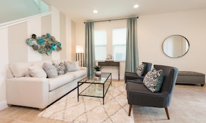A modern living room with a sofa, armchair, coffee table, and decorative wall art. - 6BR Encore Villa With Game Room & Private Pool (Kissimmee)