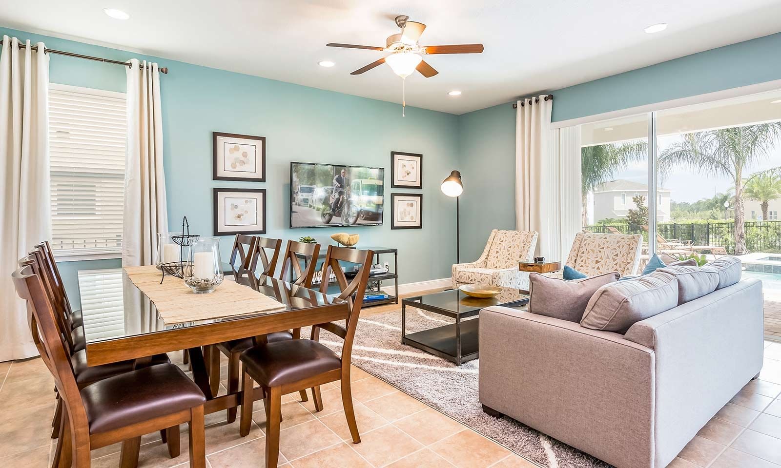 A spacious living room with a dining area, a ceiling fan, and a large window offering a view of the outdoors.