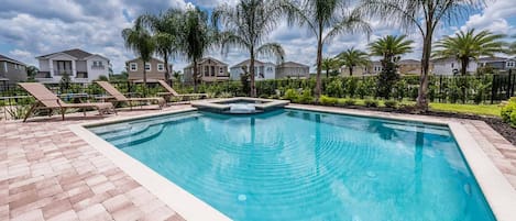 A rectangular swimming pool with a tiled deck, surrounded by palm trees and houses.