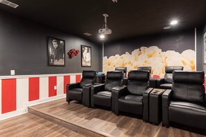 A cinema room with black leather reclining seats, a popcorn mural, and a projector ceiling light. - Chic Property With Private Pool in Encore (Kissimmee)
