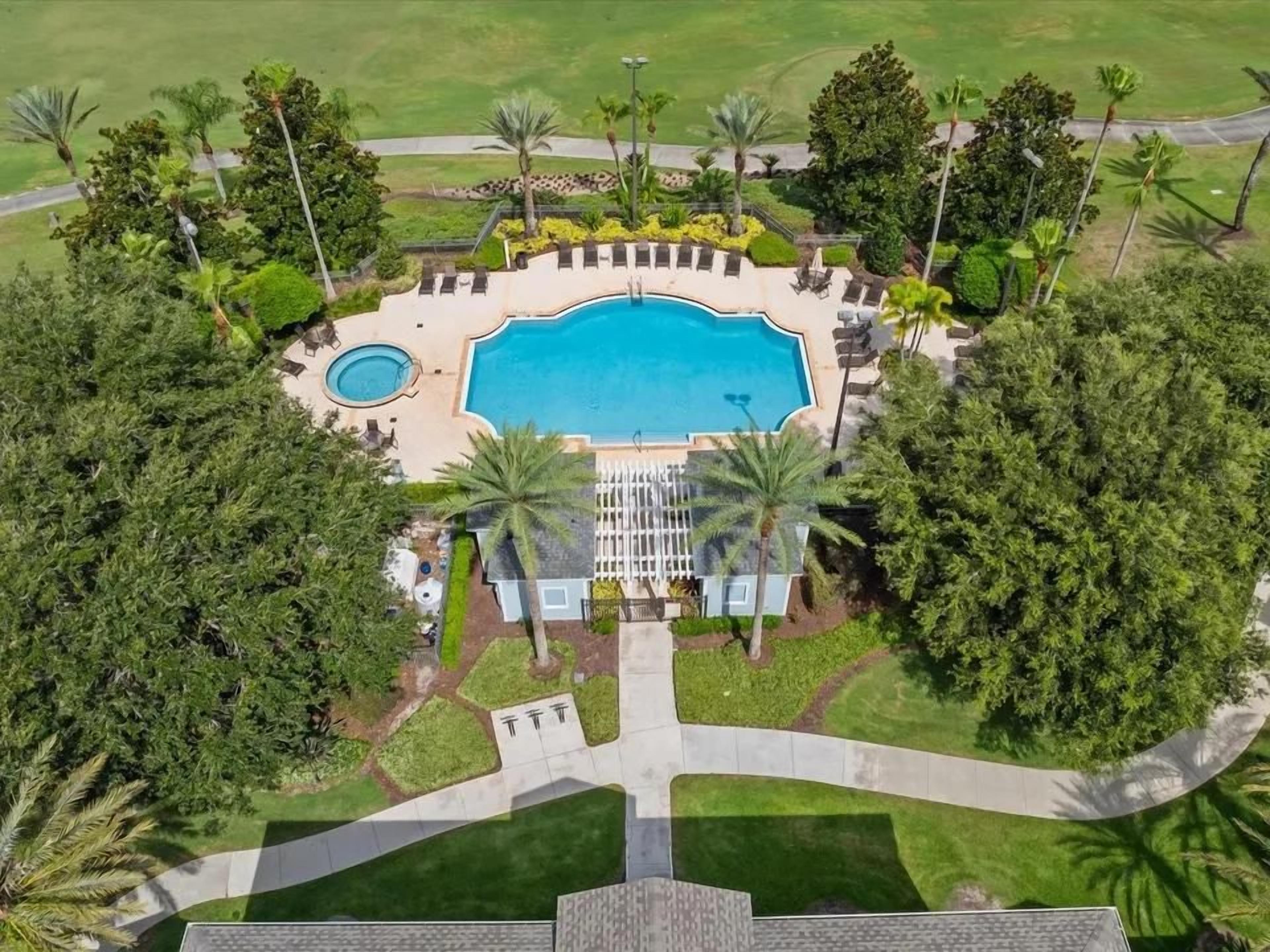 An aerial view of a resort with a central swimming pool, lounge areas, and palm trees.