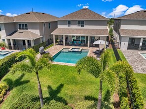 A residential property with a swimming pool, a covered patio, and a well-maintained lawn with palm trees. - Elegant Villa With Games Room at Encore (Kissimmee)