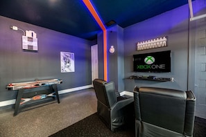 A gaming room with a mounted Xbox One, two black leather chairs, a table with a racing game, and a poster on the wall. - Elegant Villa With Games Room at Encore (Kissimmee)