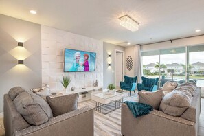 A modern living room with a flat-screen TV, comfortable seating, and a view of the outdoors. - Elegant Villa With Games Room at Encore (Kissimmee)