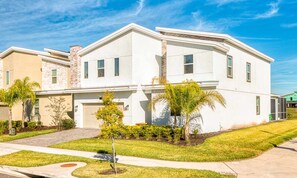 A modern two-story house with a garage, surrounded by well-maintained lawns and palm trees. - 8BR Championsgate Theater, Arcade & Pool (Davenport)