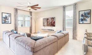 A modern living room with a large L-shaped sectional sofa, a ceiling fan, and artwork on the walls. - 8BR Championsgate Theater, Arcade & Pool (Davenport)