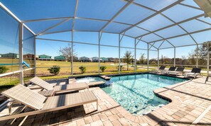 A covered outdoor swimming pool with lounge chairs and a view of a golf course. - 8BR Championsgate Theater, Arcade & Pool (Davenport)