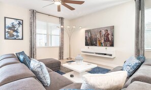 A modern living room with grey sofas, a white coffee table, and a mounted TV. - 8BR Championsgate Theater, Arcade & Pool (Davenport)