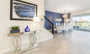 A modern interior with a staircase, a dining area, and a large window offering a view of the outdoors. - 8BR Championsgate Theater, Arcade & Pool (Davenport)
