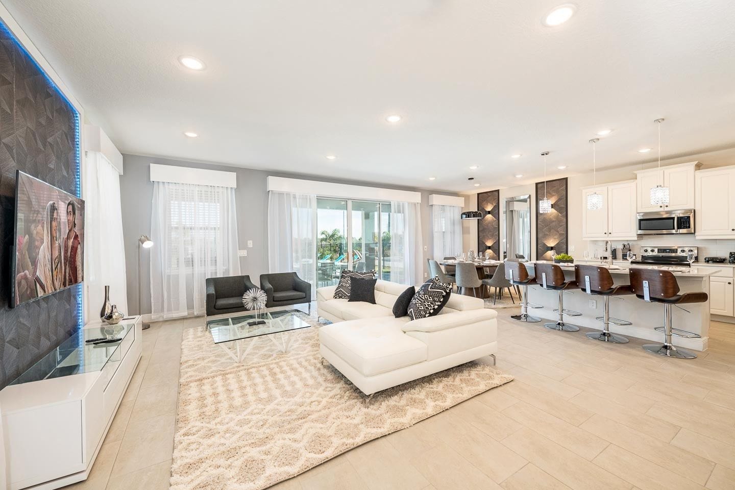 A modern living room with a white sofa, a glass coffee table, and a kitchen area with white cabinets and a dining set.