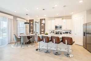 A modern kitchen with white cabinets, stainless steel appliances, and a central island with bar stools. - Dainty Home With Themed Bedrooms at Encore (Kissimmee)