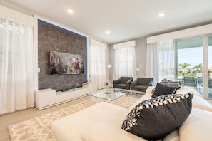 A modern living room with a flat-screen TV, two armchairs, a glass coffee table, and a sofa with patterned cushions. - Dainty Home With Themed Bedrooms at Encore (Kissimmee)