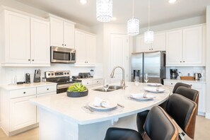 A modern kitchen with white cabinetry, stainless steel appliances, and a central island with seating. - Dainty Home With Themed Bedrooms at Encore (Kissimmee)